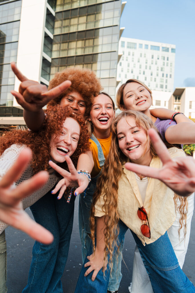 Fünf junge Frauen lachen in die Kamera und zeigen mit ihren Händen Peace-Zeichen.