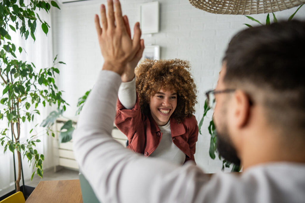 Eine junge, lachende Frau gibt einem gegenübersitzenden Mann ein High Five.